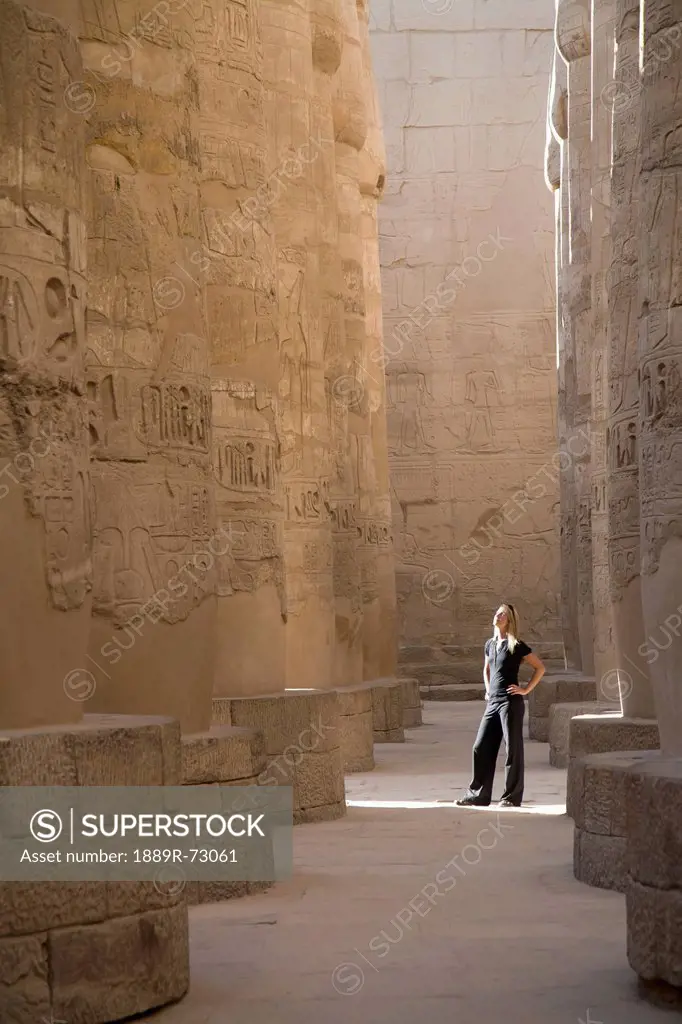 A Woman Tourist Stands At The Base Of The Massive Columns In The Temples Of Karnak On The East Bank Of Luxor Along The Nile River, Luxor Egypt