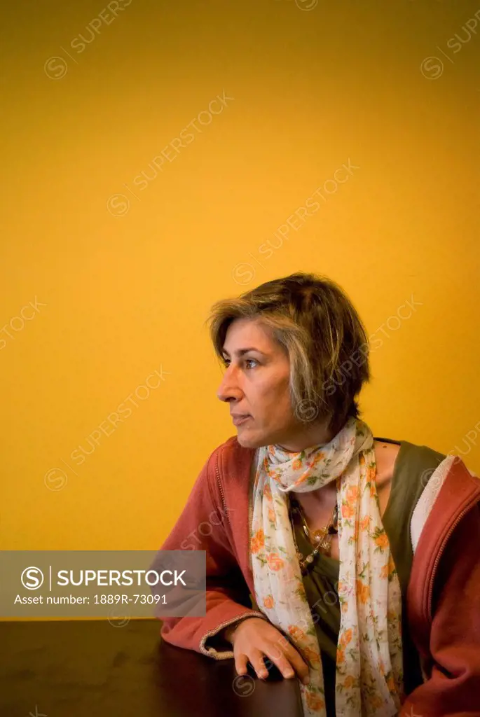 Woman Sitting At A Table Against An Orange Wall Looking Sideways, Calgary Alberta Canada