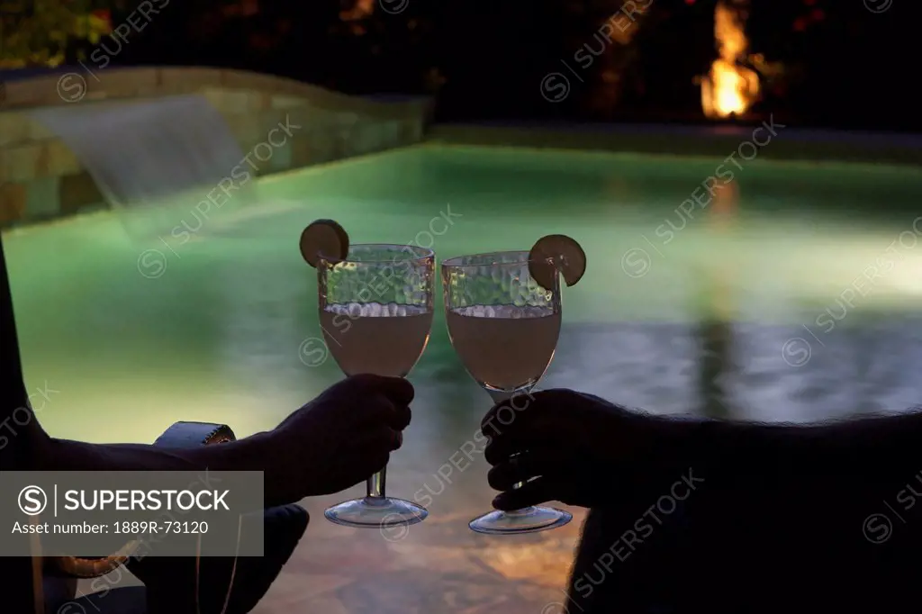 Couple Sitting At Pool Side At Night With Two Glasses Together With Lime Wedges And Pool Lights, Palm Springs California United States Of America