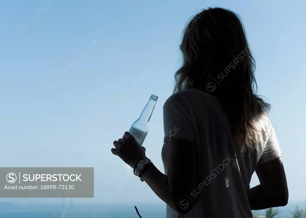 A Young Woman Drinks A Beverage From A Glass Bottle While Looking Out To The Ocean, Tarifa Cadiz Andalusia Spain