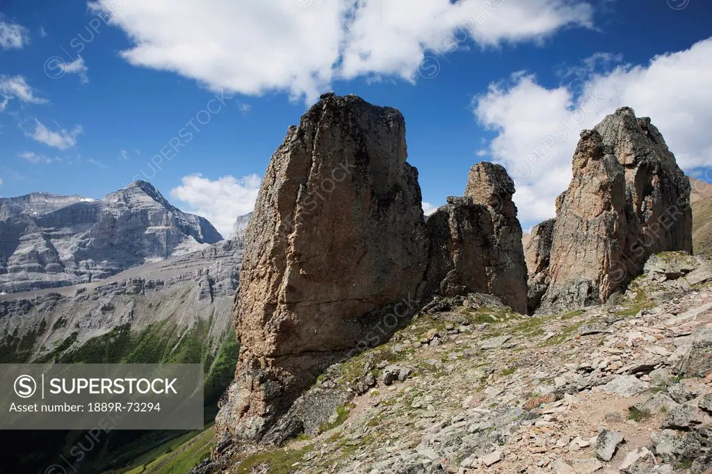 Large Rock Sentinels On Mountain Ridge With A Mountain Range And Valley In The Background With Blue Sky And Clouds, Alberta Canada