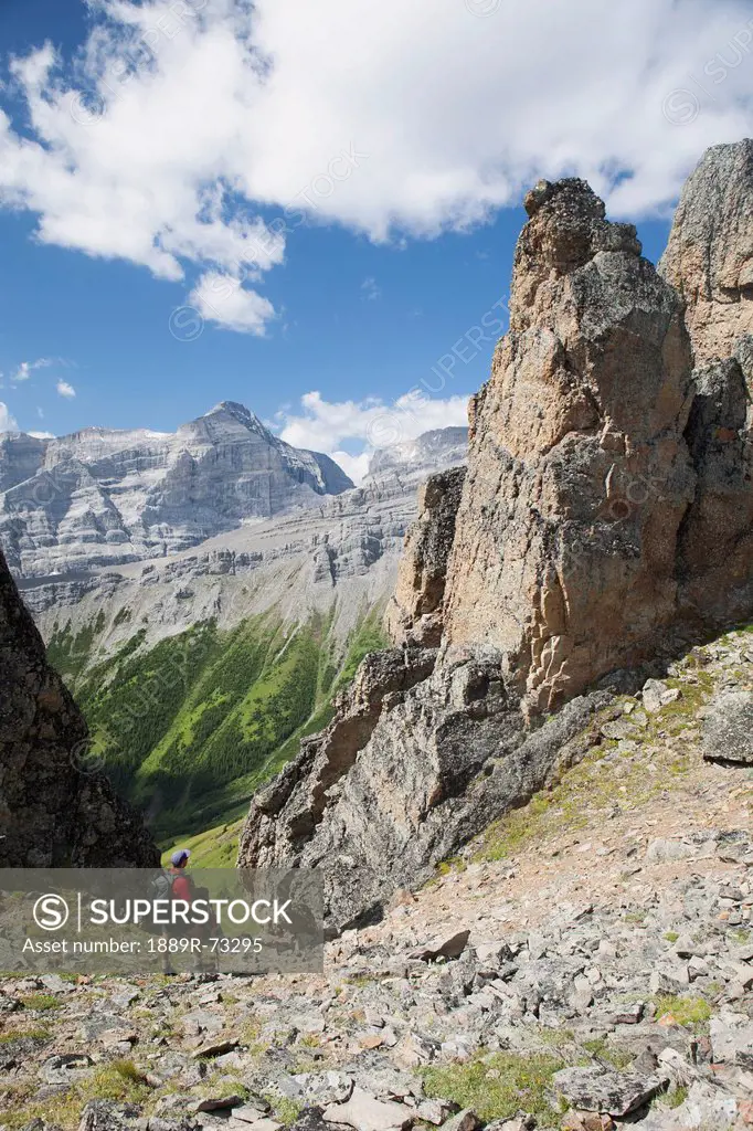 Male Hiker In The Distance On Rocky Trail With Large Sentinels And Mountains In The Background With Blue Sky And Clouds, Alberta Canada