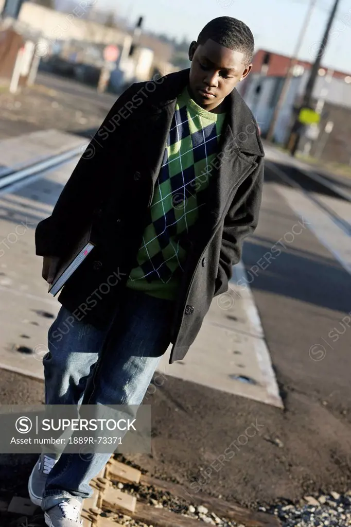 Teenage boy holding a school book and walking on train tracks, portland oregon united states of america