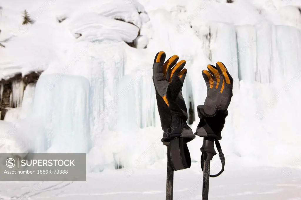 Close up of cross_country ski gloves on top of poles with a frozen ice wall and snow covered cliffs in the background, alberta canada