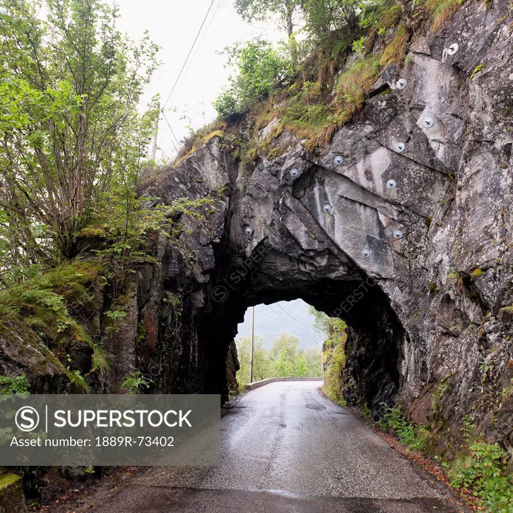A wet road leading through a tunnel in a rock cliff, bergen norway