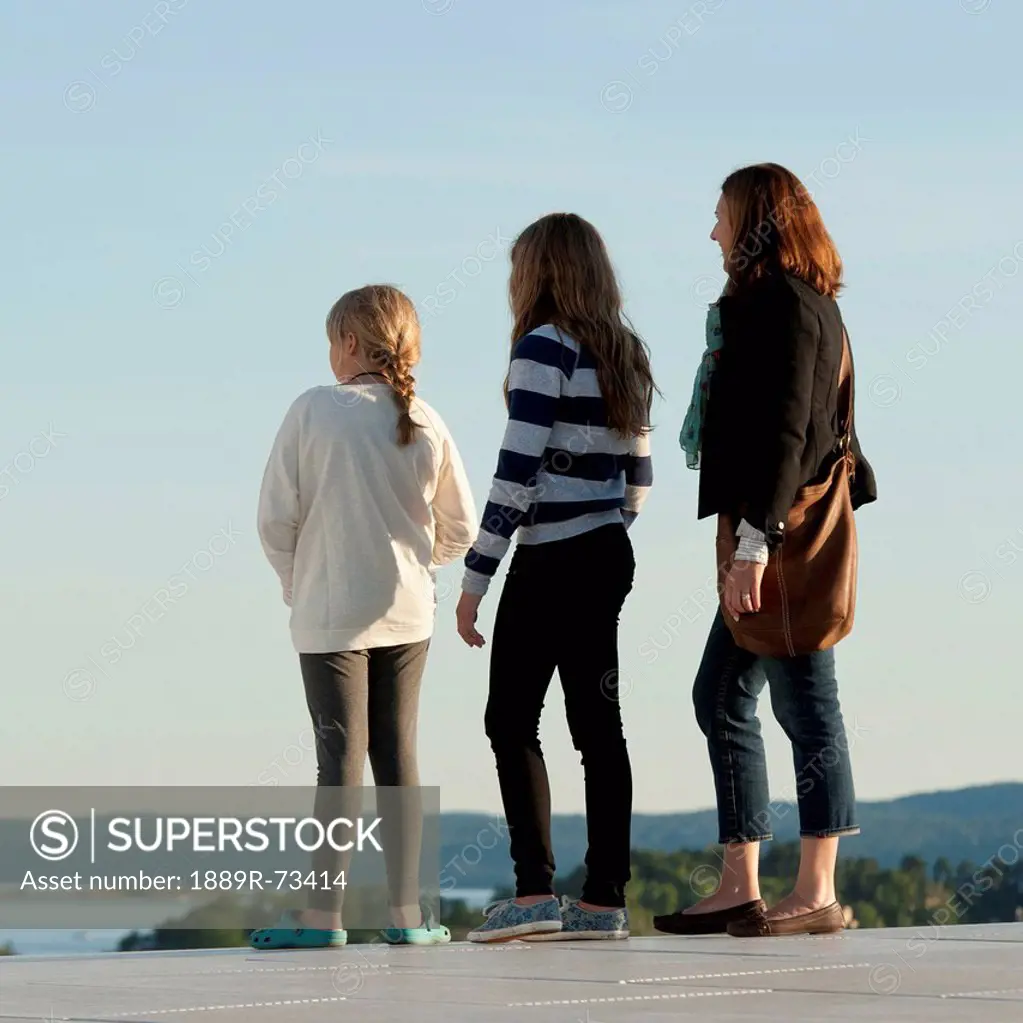 A mother and two daughters stand looking out over the water, oslo norway