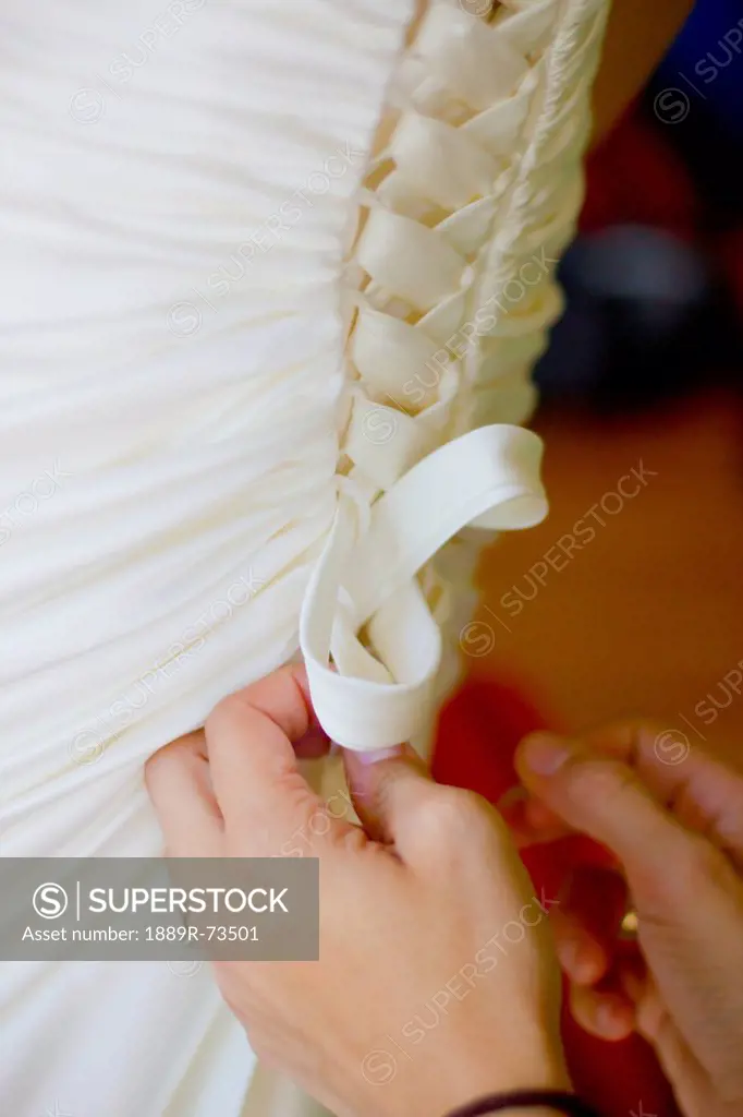 Hands fastening the laces on the back of a bride´s gown, vancouver british columbia canada