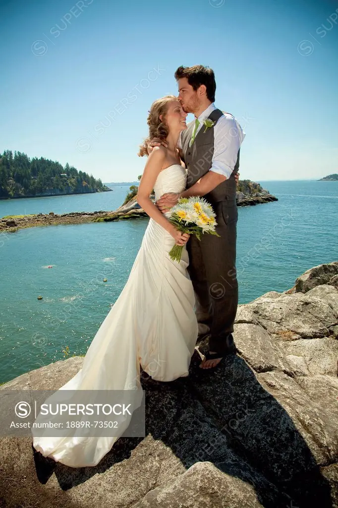 A bride and groom embrace at the water´s edge in whytecliff park, vancouver british columbia canada