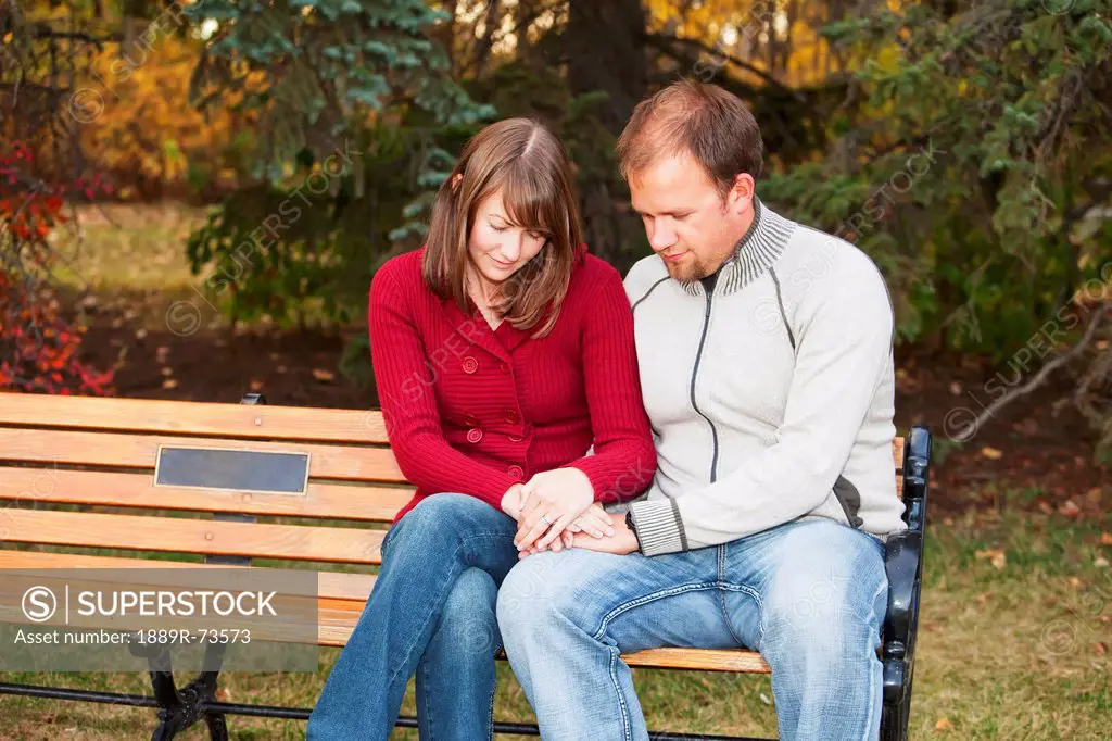 Young Married Couple Praying Together On A Park Bench, Edmonton Alberta Canada