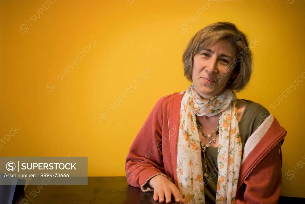 Woman Seated At A Wooden Table Against An Orange Wall, Calgary Alberta Canada
