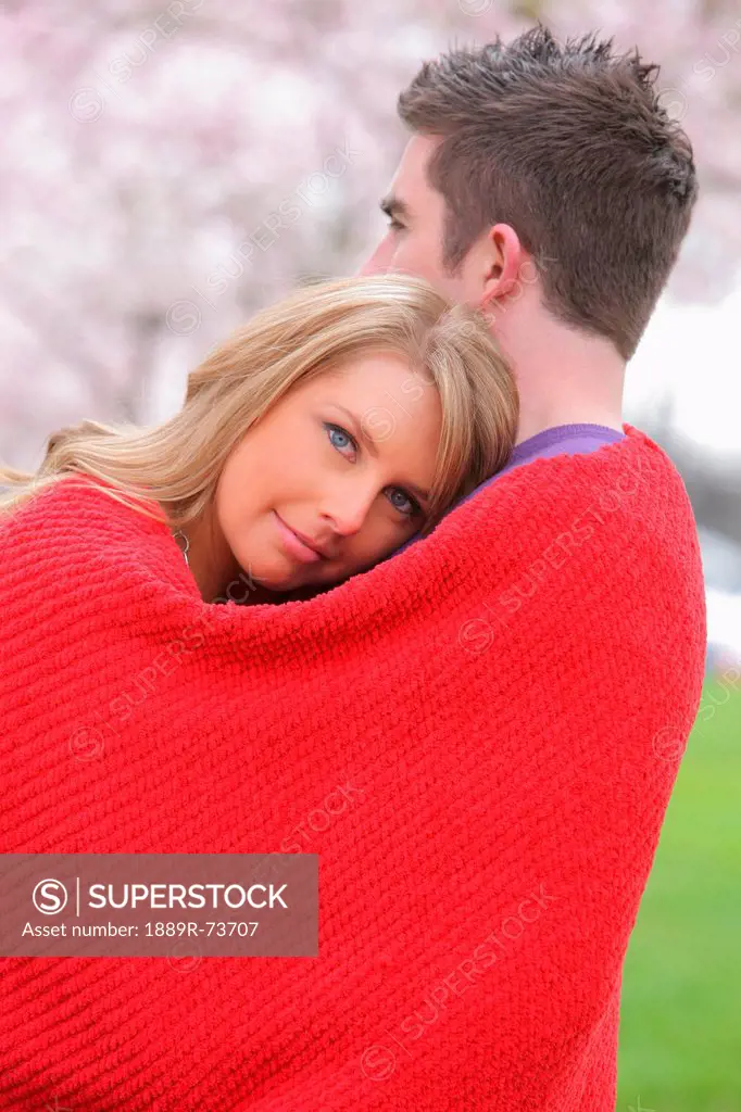 Couple Cuddled Up In A Red Blanket With Young Woman Looking At The Camera, Portland Oregon United States Of America