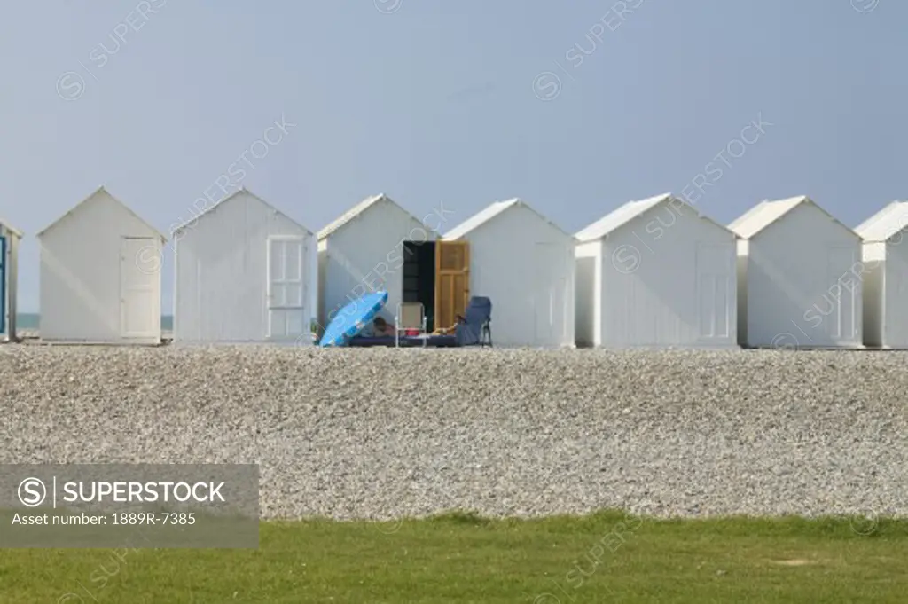 A blue umbrella and lounge chair in front of z white beach cabin on Cayeux sur-Mer, France