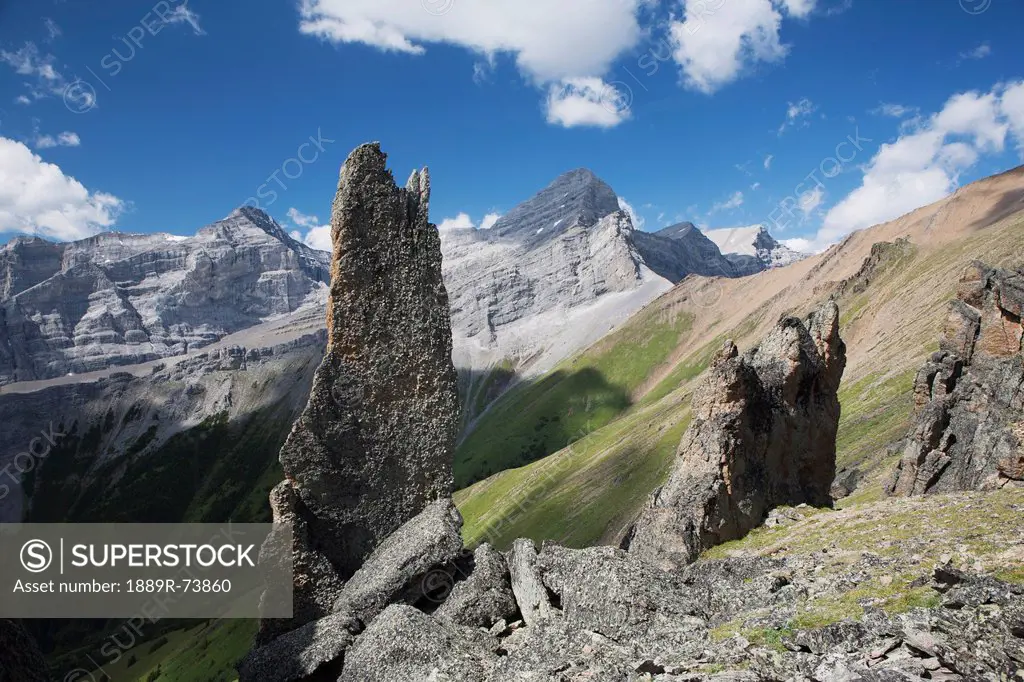 Large Rock Sentinels On Mountain Ridge With A Mountain Range And Valley In The Background With Blue Sky And Clouds, Alberta Canada