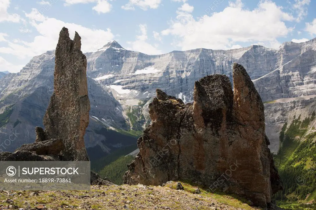Large Rock Sentinels On Mountain Ridge With A Mountain Range In The Distance With Blue Sky And Clouds, Alberta Canada