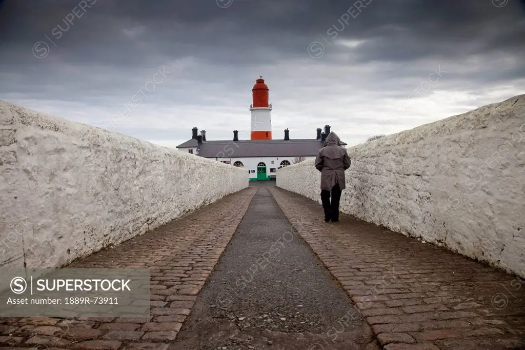 Person walking on a paved walkway towards a lighthouse, south shields tyne and wear england