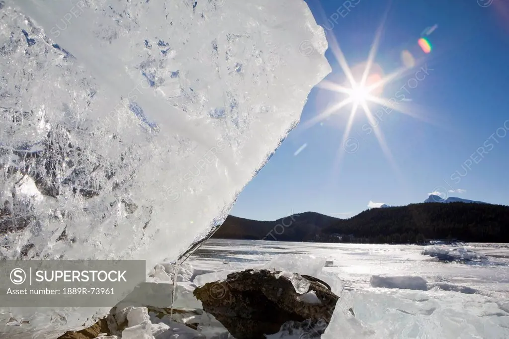 Ice formation on shoreline of a mountain lake with a sunburst and blue sky, banff alberta canada