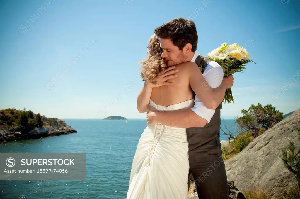 A bride and groom embrace at the water´s edge in whytecliff park, vancouver british columbia canada