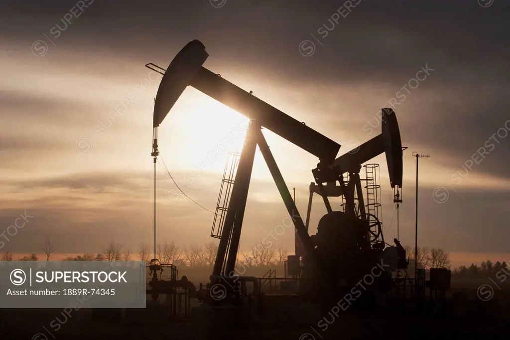 Silhouette Of Two Pump Jacks At Sunrise With Clouds, Alberta Canada