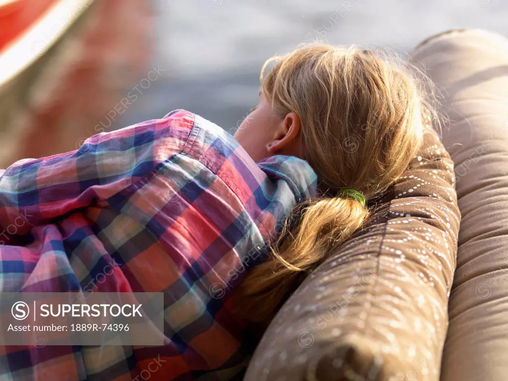 A girl rests on a cushioned couch outdoors beside the water, lake of the woods ontario canada