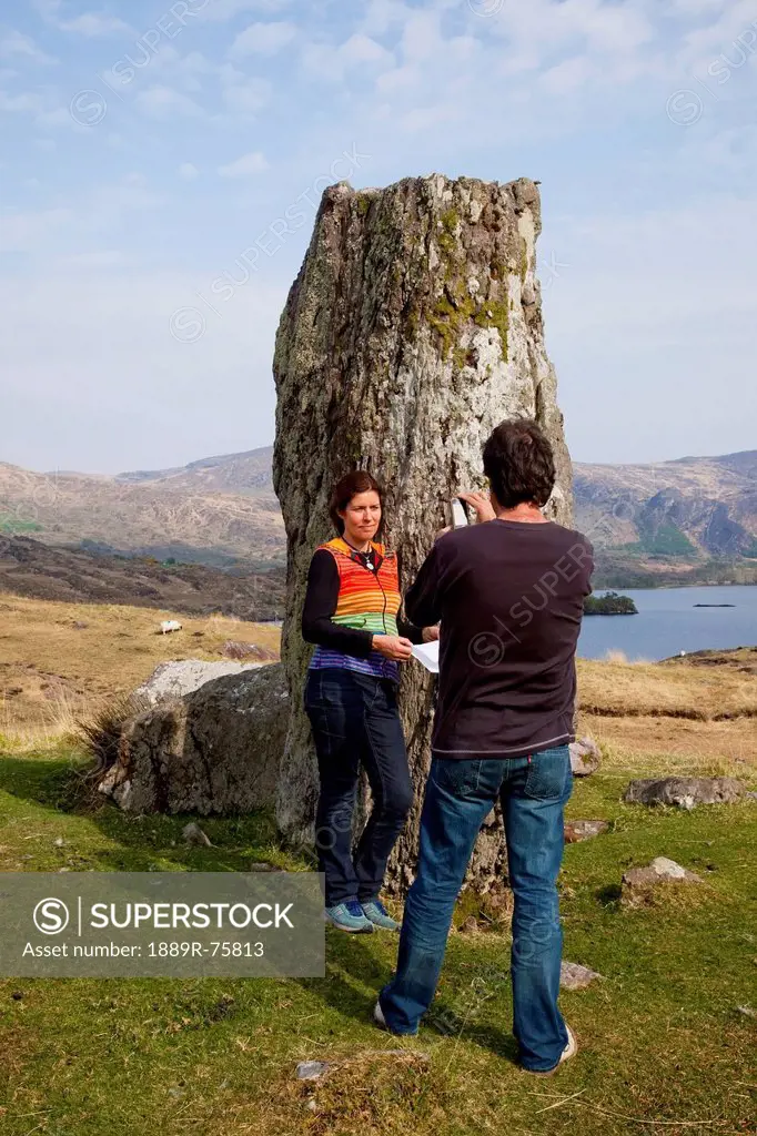 A Man Taking A Picture Of A Woman Beside A Rock Formation On The Coast Near Kenmare, County Kerry Ireland