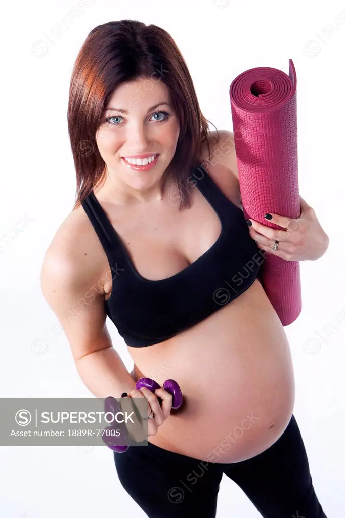 A pregnant woman holding her workout mat and dumbbell weights, edmonton alberta canada