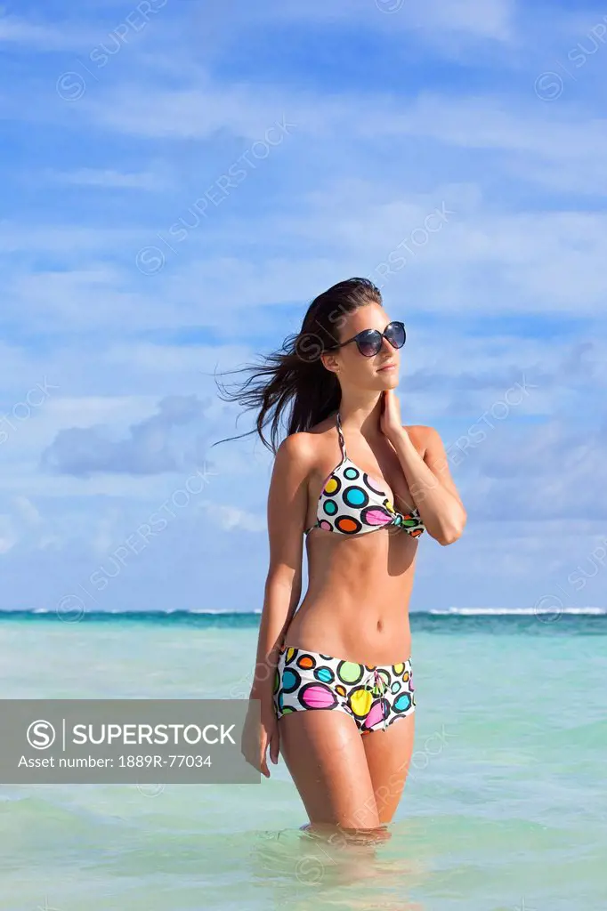 A woman standing in the ocean wearing a colourful bikini and sunglasses, punta cana la altagracia dominican republic