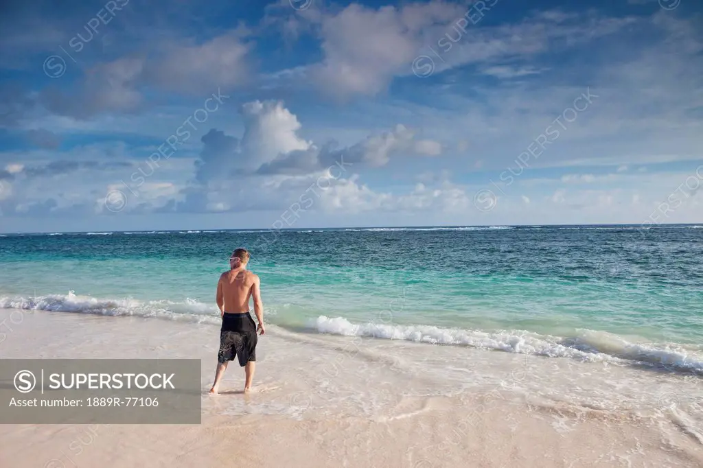 A man stands on a beach with the water washing up on his feet, punta cana la altagracia dominican republic