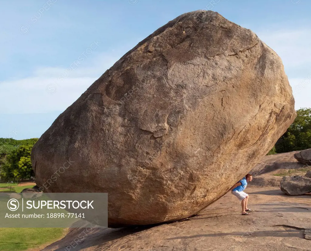 A man stands under a large boulder at arjuna´s penance, mahabalipuram tamil nadu india