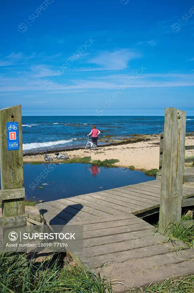A Woman Stands At The Water´s Edge Looking Out Over The Water, Northumberland England