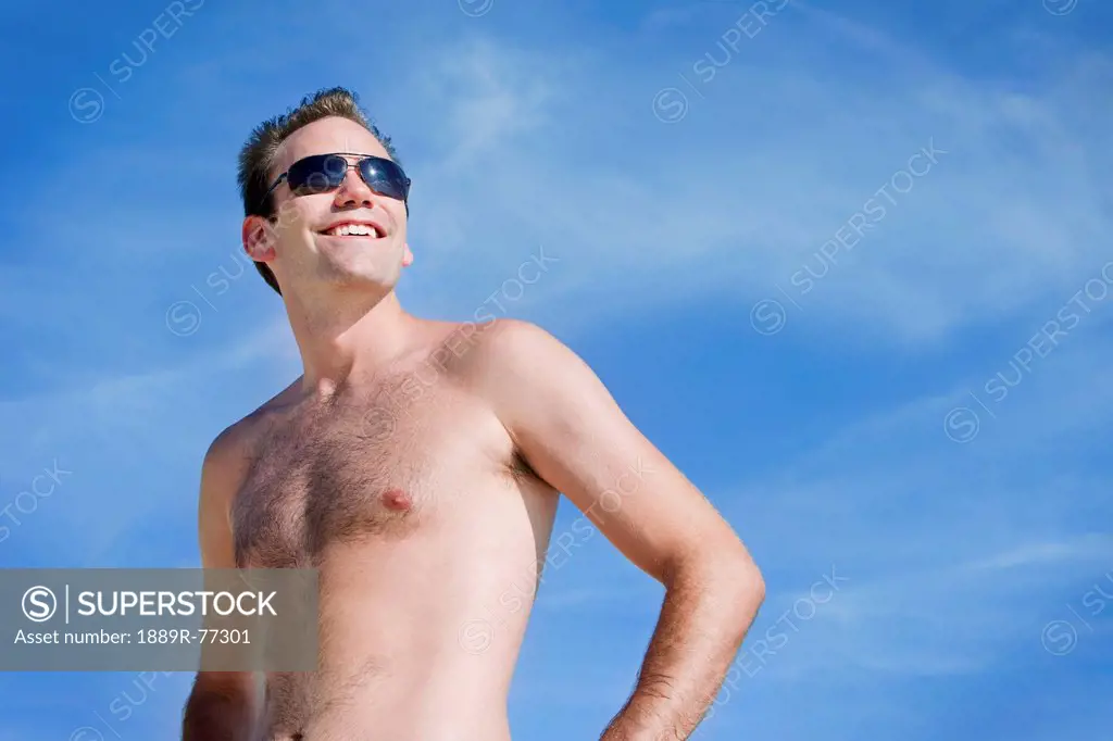 Portrait of a man wearing a swimsuit and sunglasses against a blue sky, punta cana la altagracia dominican republic