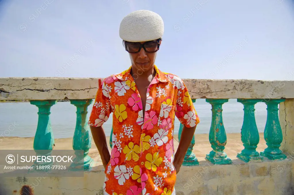 Asian man in bright flowered shirt in front of wall and ocean, puerto rico