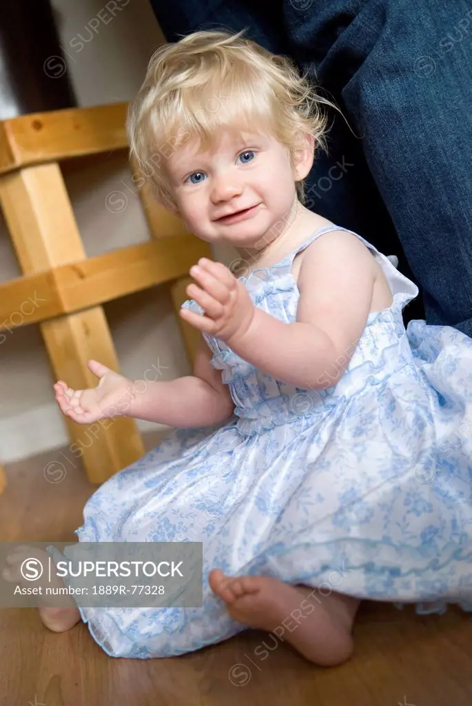 A young girl with blond hair and blue eyes sitting on the floor in a dress, millet alberta canada