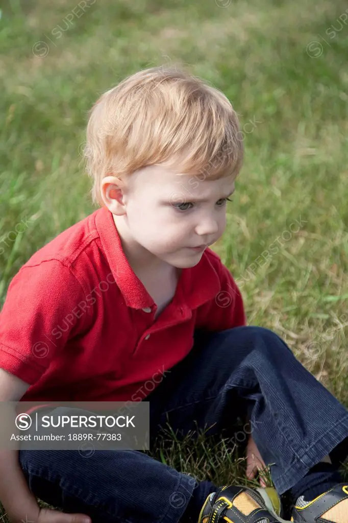 a young boy sits on the grass, edmonton, alberta, canada