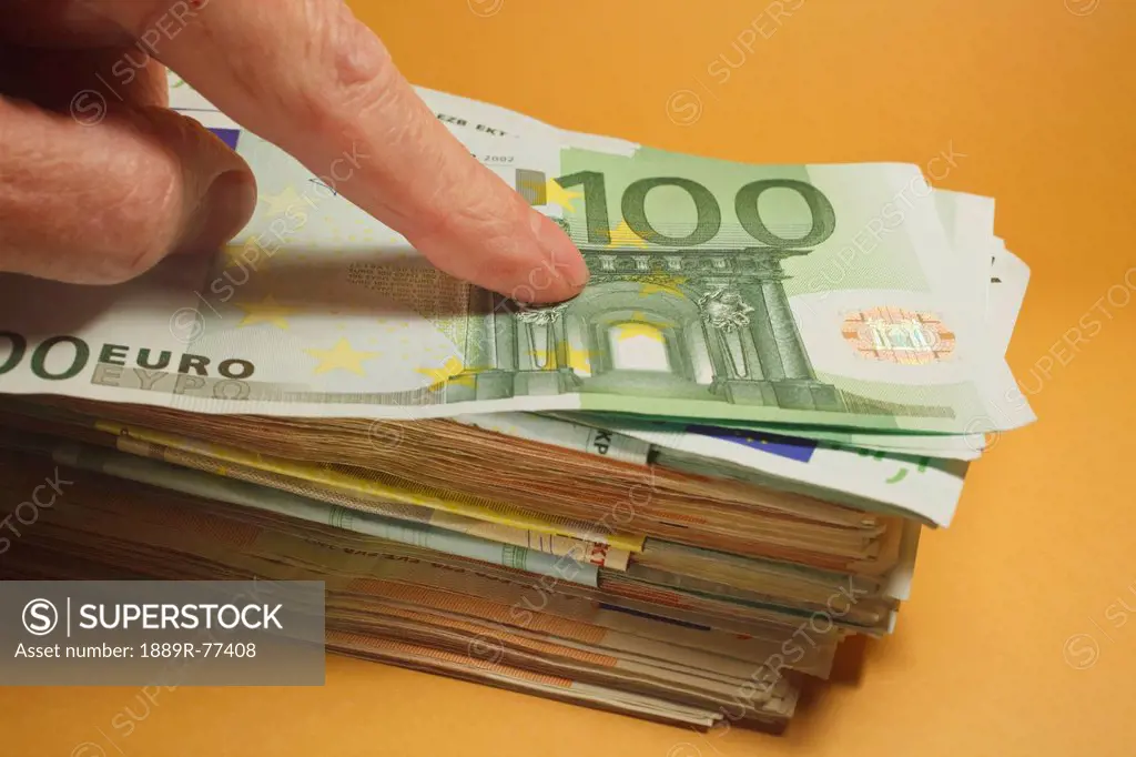 Finger pressing down on top of big pile of euro notes, spain