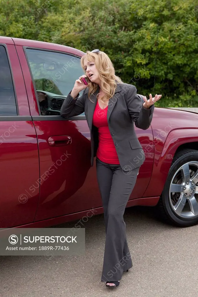 a woman makes a cell phone call while standing by her vehicle, edmonton, alberta, canada