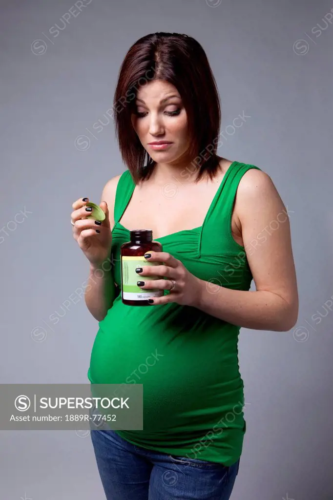 A pregnant woman looks curiously into an open bottle of vitamins, edmonton alberta canada