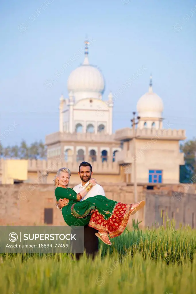 Portrait of a mixed race couple her wearing a sari with a temple in the background, ludhiana punjab india