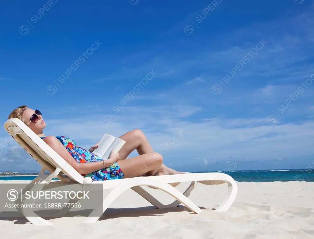 A woman relaxing with a book on a beach chair by the ocean, punta cana la altagracia dominican republic