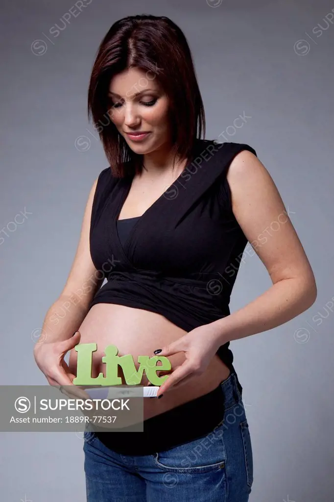 A pregnant woman holds us a pregnancy test and a sign saying ´live´ beside her bare pregnant belly, edmonton alberta canada