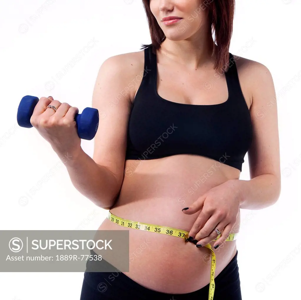 A pregnant woman holds a measuring tape to her belly while lifting a dumbbell, edmonton alberta canada