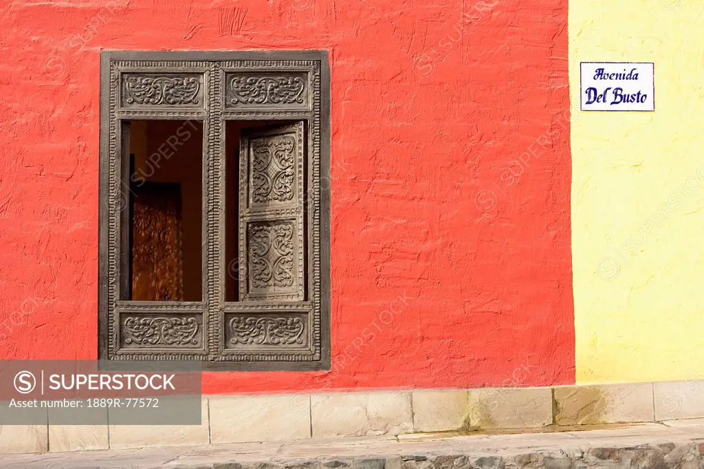 A window with ornate gold trim and shutters on a building painted red and yellow, lima peru