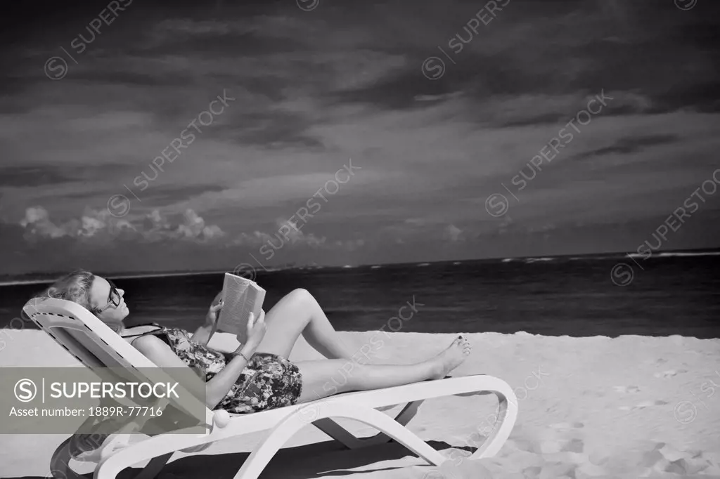 A woman sits reading in a lounge chair on the beach, punta cana la altagracia dominican republic