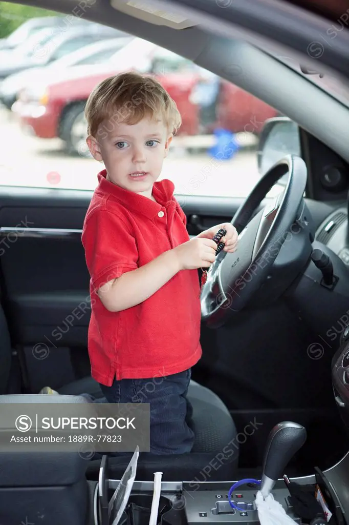a young boy sits by the steering wheel in the front seat of a car, edmonton, alberta, canada