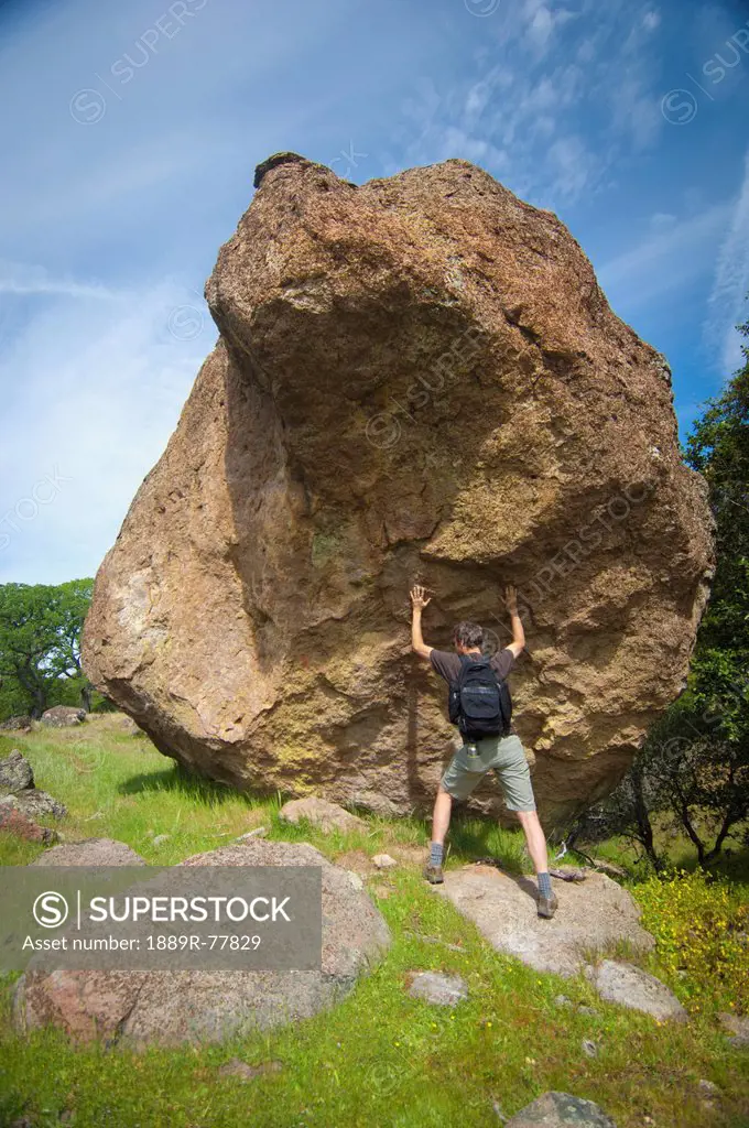 Man with backpack pushing against large boulder, sutter buttes california united states of america
