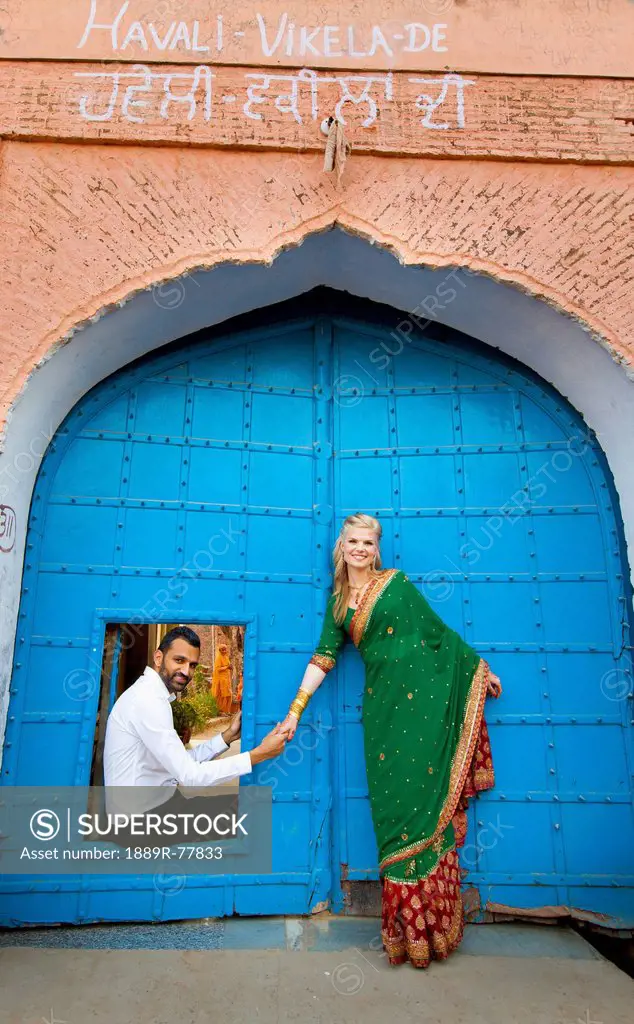 A mixed race couple with her wearing a sari at a doorway with large blue doors, ludhiana punjab india