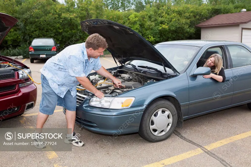 A man helps boost the car battery of a woman´s car in a parking lot, edmonton alberta canada