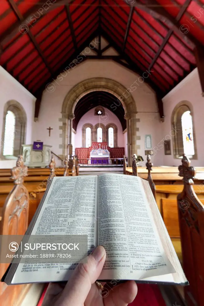 A hand holds a small open bible at the back of a church, howick northumberland england