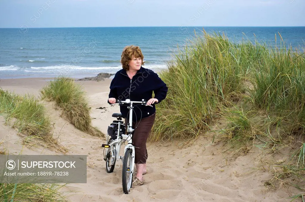 A Woman With Her Bike In The Sand Along The Water, Northumberland England