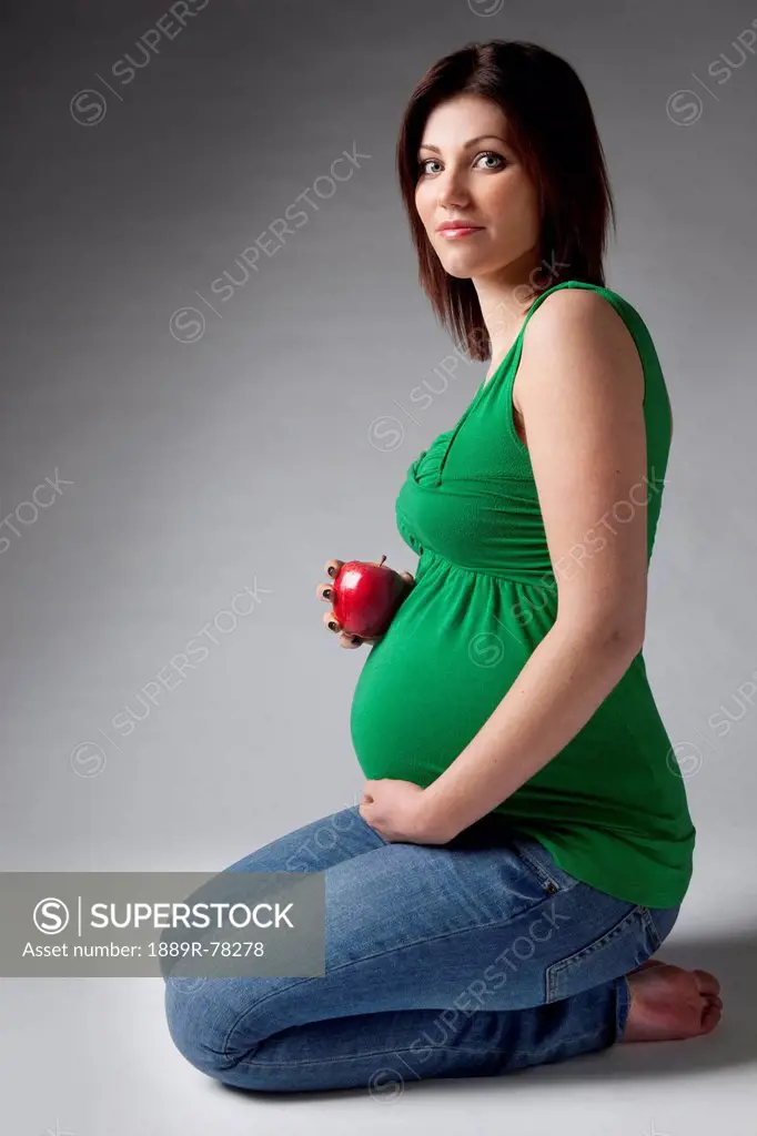 A pregnant woman holding an apple beside her pregnant belly, edmonton alberta canada