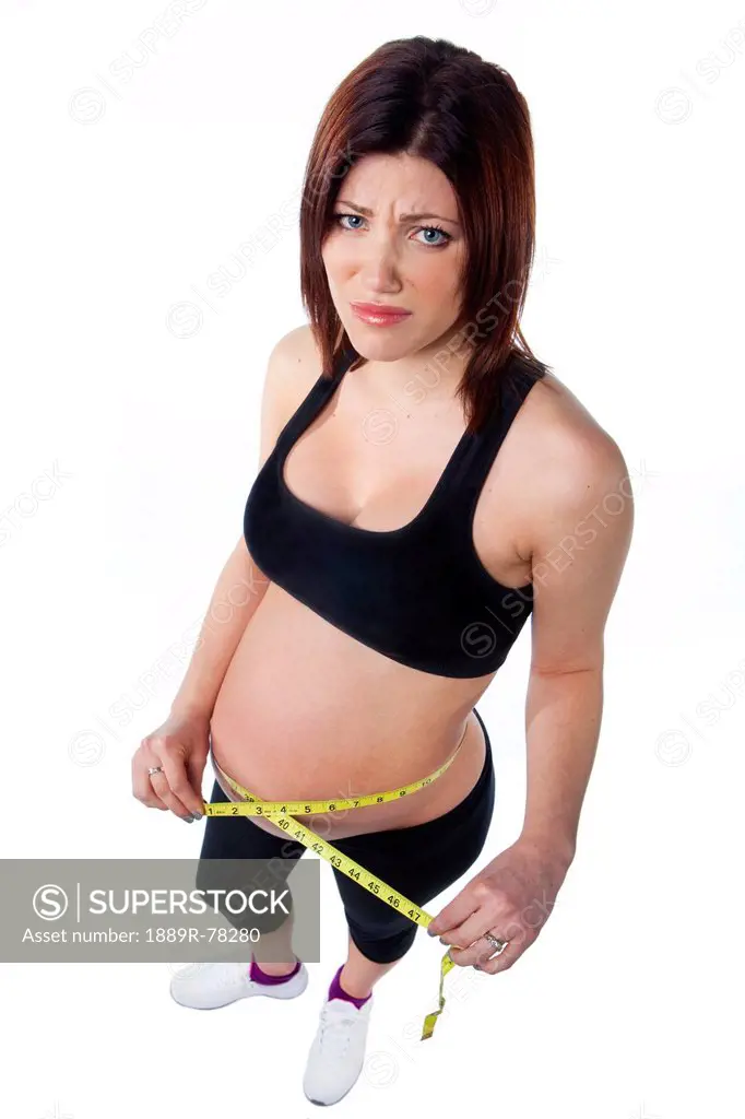 A pregnant woman holds a measuring tape around her bare pregnant belly, edmonton alberta canada